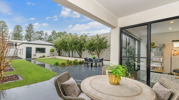 Relax in a serene outdoor space with a patio table and two chairs, surrounded by lush greenery and a beautiful lawn.