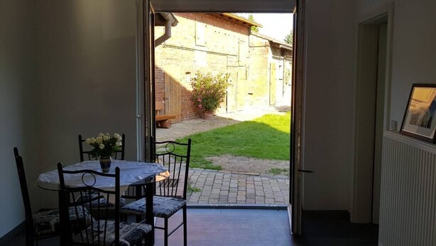 An open door leading to a patio with a table and chairs, a small garden, and a framed picture on the wall. - Vacation apartment in Cottbus-Klein Ströbitz near the bathing lake (Cottbus)