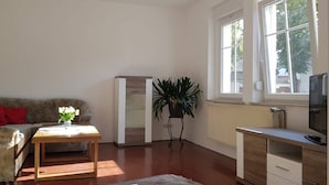 A living room with a sofa, a coffee table, a TV, a radiator, and a window. - Vacation apartment in Cottbus-Klein Ströbitz near the bathing lake (Cottbus)