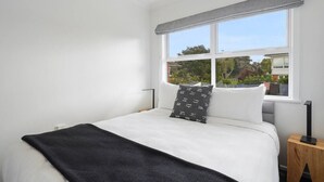 A bedroom with a large bed, a window with a view of greenery, and a bedside table with a lamp.