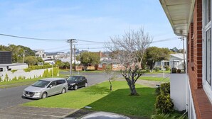 A residential street with two parked cars, a grassy lawn, and houses with brick and white exteriors.