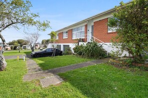 A residential house with a brick exterior, a front yard with a pathway, and a black car parked in the driveway.