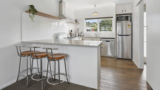 A modern kitchen with white cabinets, stainless steel appliances, a large island with bar stools, and a window providing a view of the outdoors.