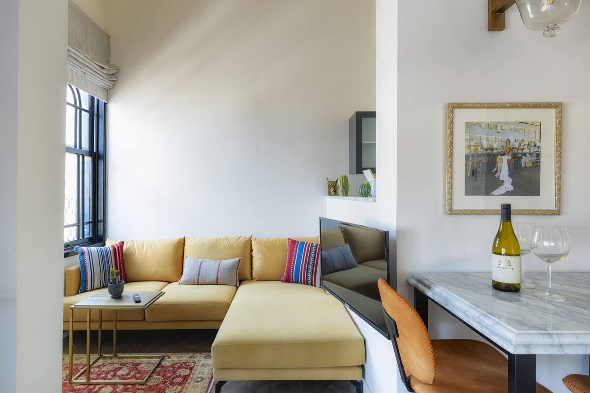 A modern living room with a sofa, a small table, a wine bottle, and a framed picture on the wall.
