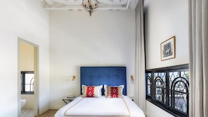 Een slaapkamer met een groot bed, een kroonluchter, een raam met uitzicht en een lijst met foto aan de muur.