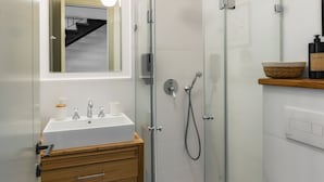 Een moderne badkamer met een douchecabine van glas, een witte wastafel met een houten opbergmeubel en een spiegel boven de wastafel.