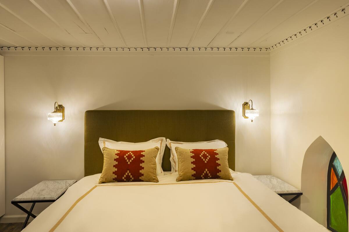 A bedroom with a large bed, two nightstands, and wall-mounted sconces.