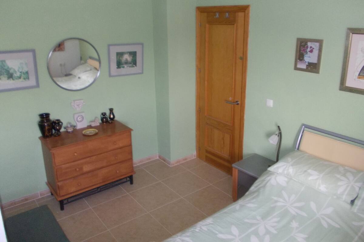 A bedroom with a bed, dresser, mirror, and a door.