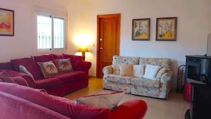 A living room with two sofas, one red and one floral, a wooden door, and a fireplace. - Casa Camino (Valle de Abdalagis)