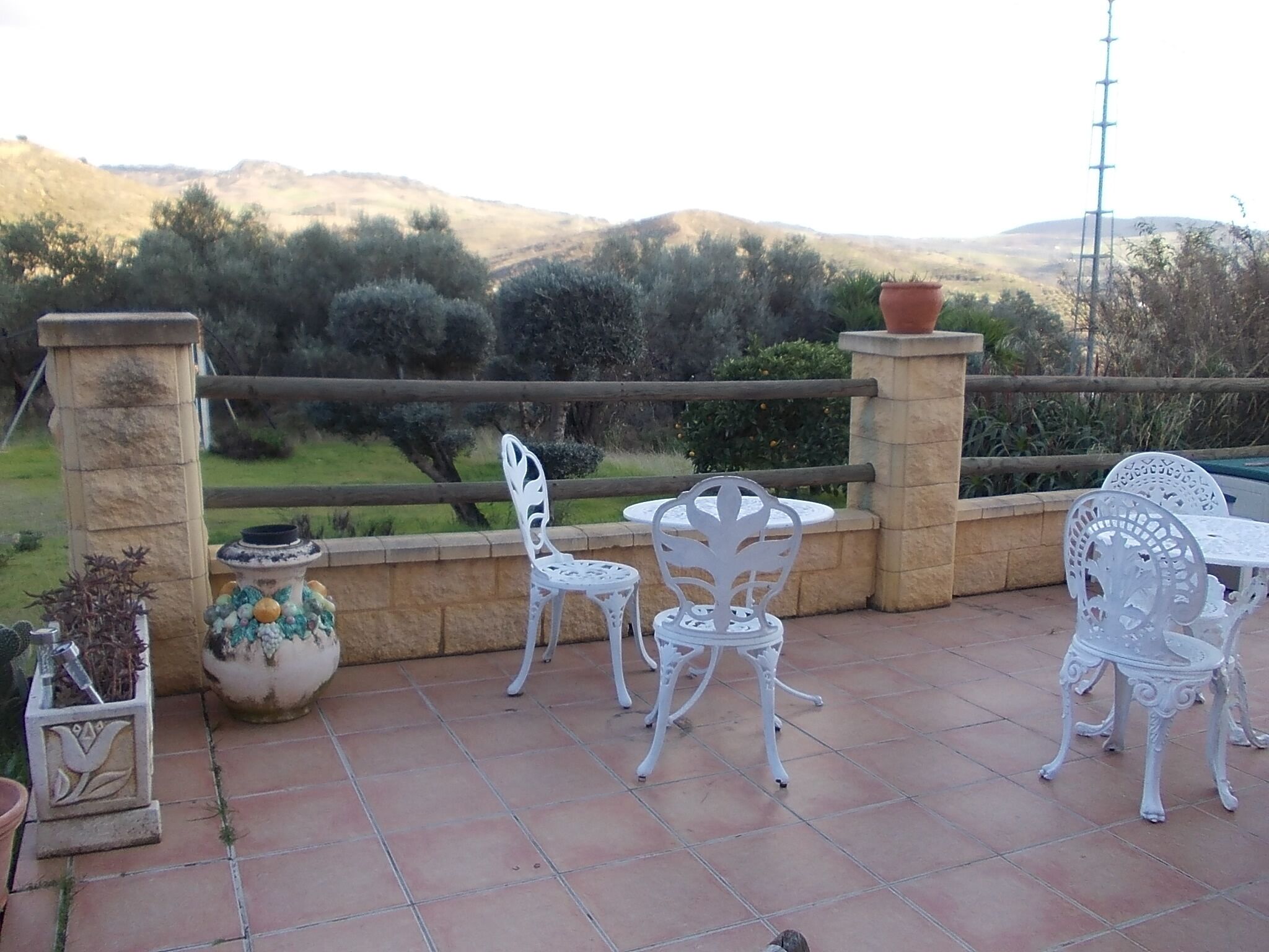 A patio with white metal chairs and a table, surrounded by stone pillars and potted plants.