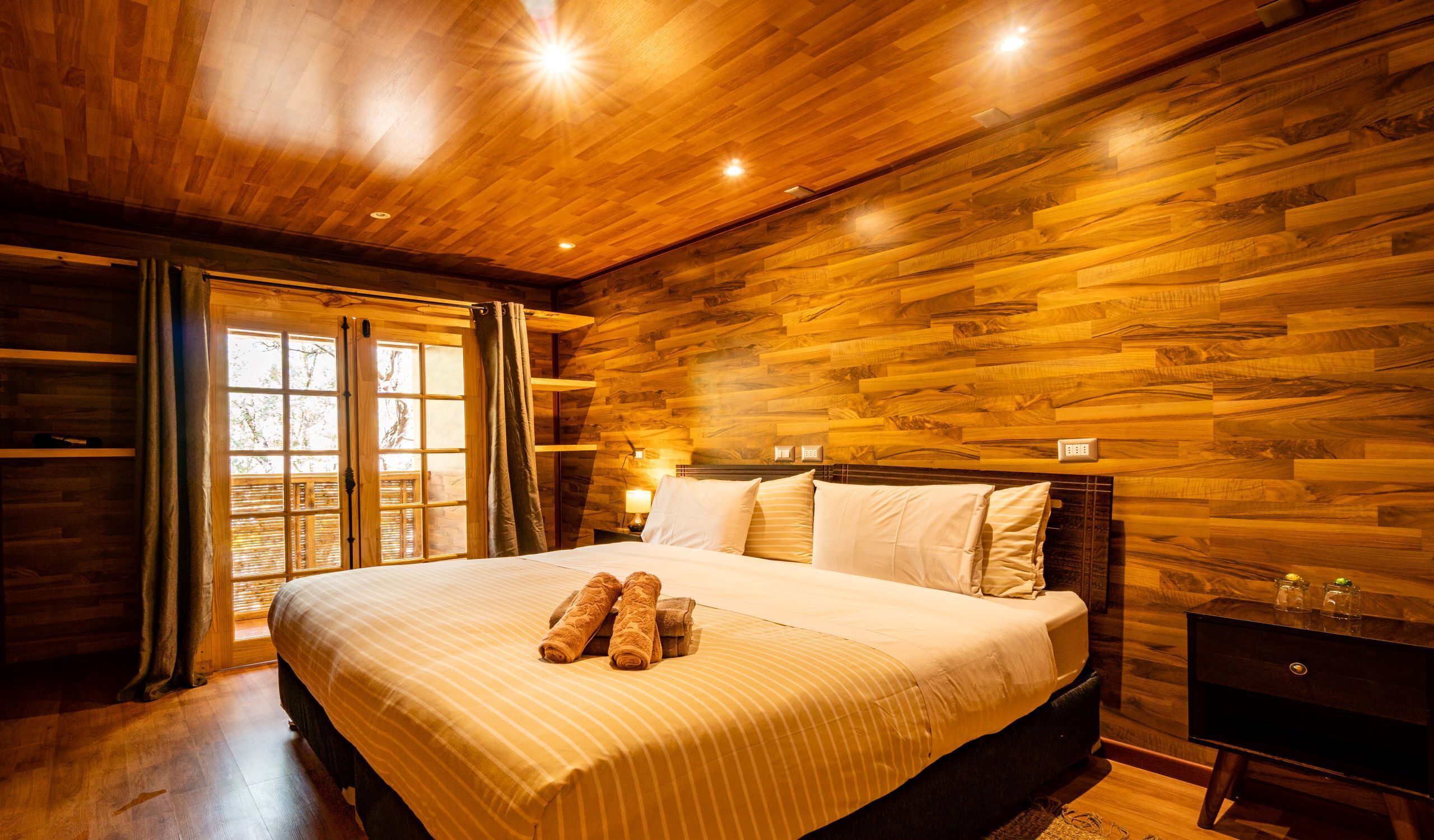 A wooden-paneled bedroom with a bed, curtains, and a nightstand.