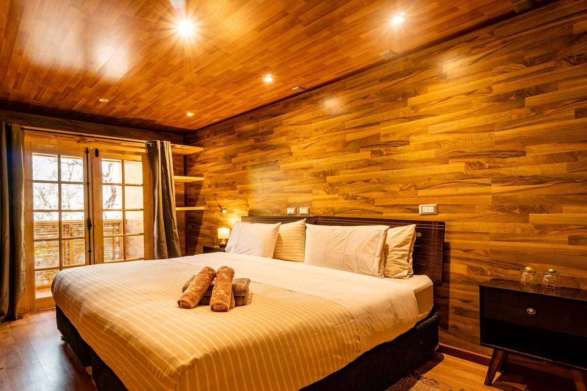 A wooden-paneled bedroom with a bed, curtains, and a nightstand.