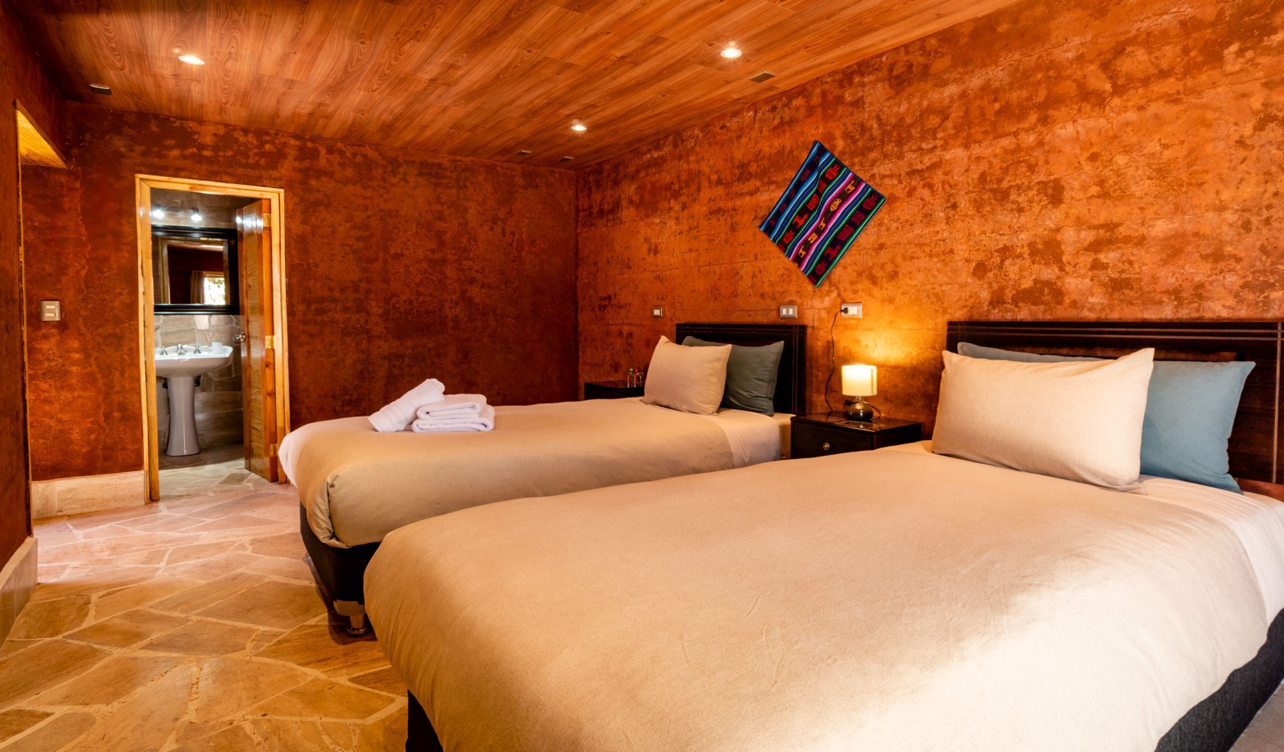 A hotel room with two beds, a bathroom, and a wooden ceiling.