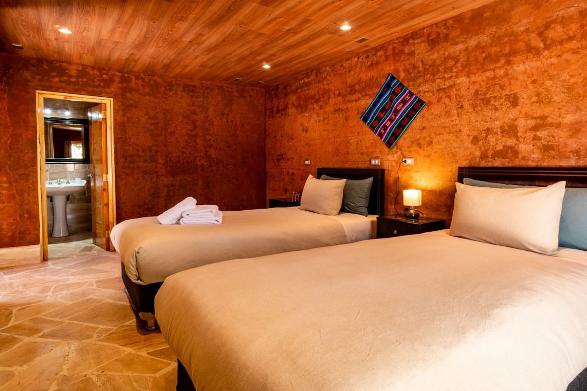 A hotel room with two beds, a bathroom, and a wooden ceiling.