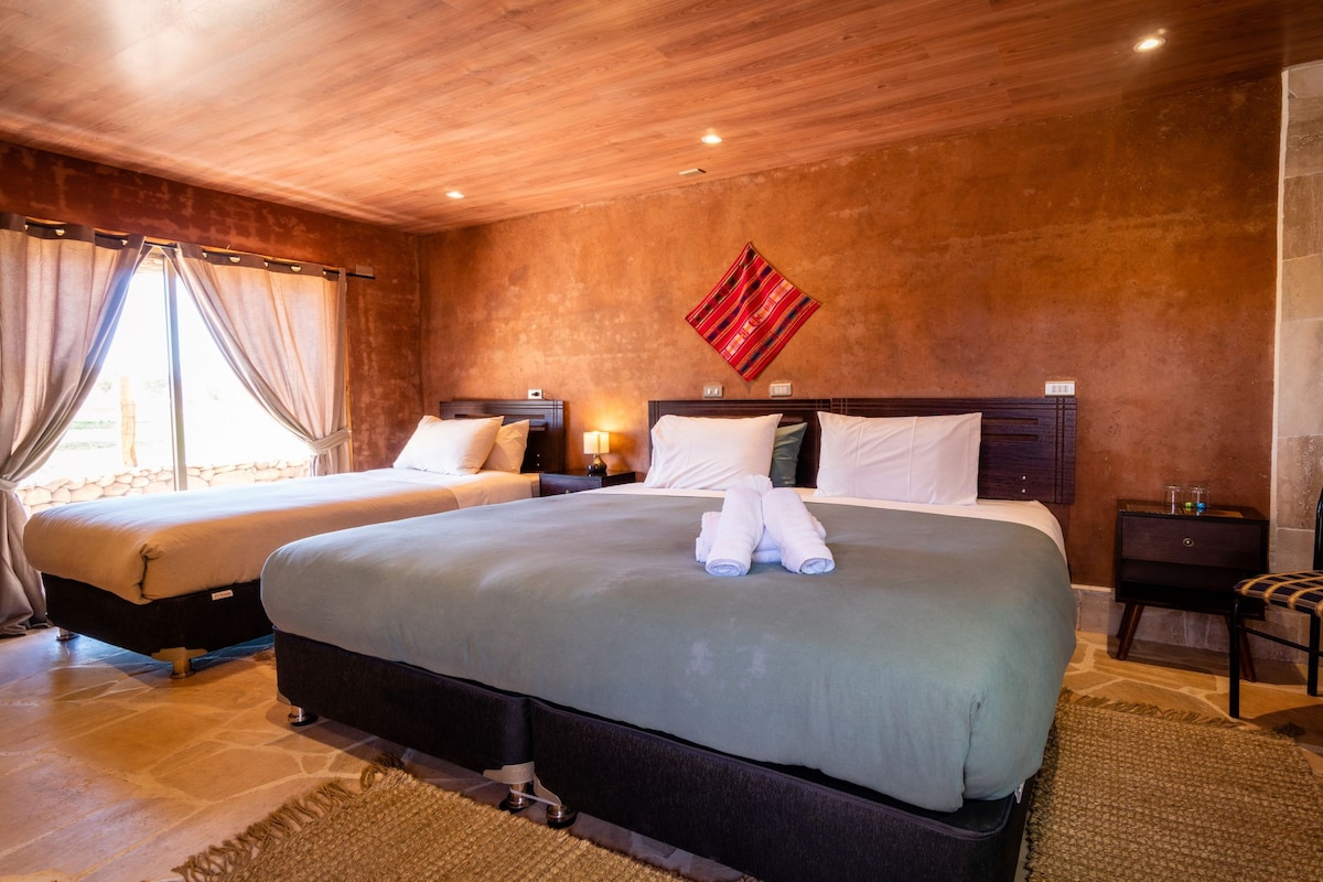 Une chambre d’hôtel avec deux lits, un mur en pierre, un plafond en bois et un élément décoratif rouge.