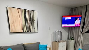A modern living room with a grey sofa, a wooden side table, a small round table, and a TV mounted on the wall.