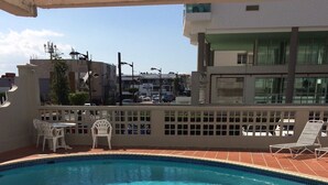 A rooftop pool with clear blue water, surrounded by white chairs and a tiled deck.