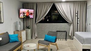 A modern living room with a sofa, two armchairs, a small table, a TV, and a bed.
