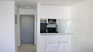A compact kitchen with a microwave, oven, and a small counter with two white stools.