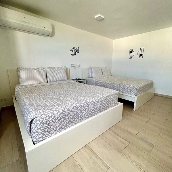 A bedroom with two beds, a nightstand, a wall-mounted air conditioner, and a ceiling light. - Beach Studio Isla Verde-Sea Dollar #3 (Carolina)