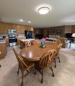 A modern kitchen with wooden cabinets, stainless steel appliances, and a dining area with a wooden table and chairs.