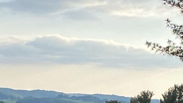 Un campo de golf con un mástil de bandera en primer plano, rodeado de árboles y colinas onduladas al fondo.