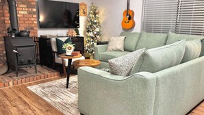 Ein gemütliches Wohnzimmer mit einem grünen Sofa, einem kleinen runden Holztisch, einem Kamin aus Backsteinen und einem Weihnachtsbaum.