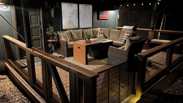 Ein gemütlicher Außenbereich mit einer Couch, Sesseln und einem Couchtisch, umgeben von einer Holzterrasse und einem Grill.