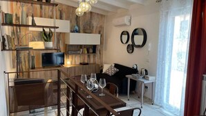 A cozy living area with a dining table set for four, a sofa, and a coffee table. There are decorative items on shelves, a television, and a window with curtains. - DOMUS TUSCIA APARTMENTS Via Estrema 2 (Viterbo)