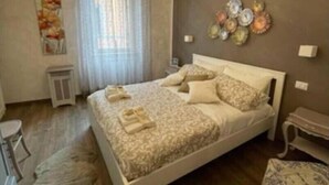 A bedroom with a large bed, a chandelier, a wall art piece, and a small side table. - DOMUS TUSCIA APARTMENTS Via Estrema 2 (Viterbo)