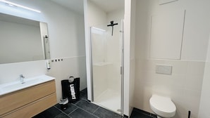 A modern bathroom with a glass shower enclosure, a white toilet, and a wooden vanity. - APSTAY Apartments (Graz)