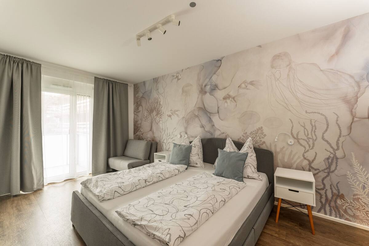 Un dormitorio con una cama grande, una mesita de noche, una silla y un mural en la pared.