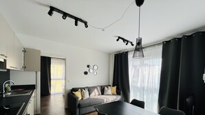 A modern kitchen with integrated appliances, a dining area with a table and chairs, a sofa with cushions, and a large window with curtains. - APSTAY Apartments (Graz)