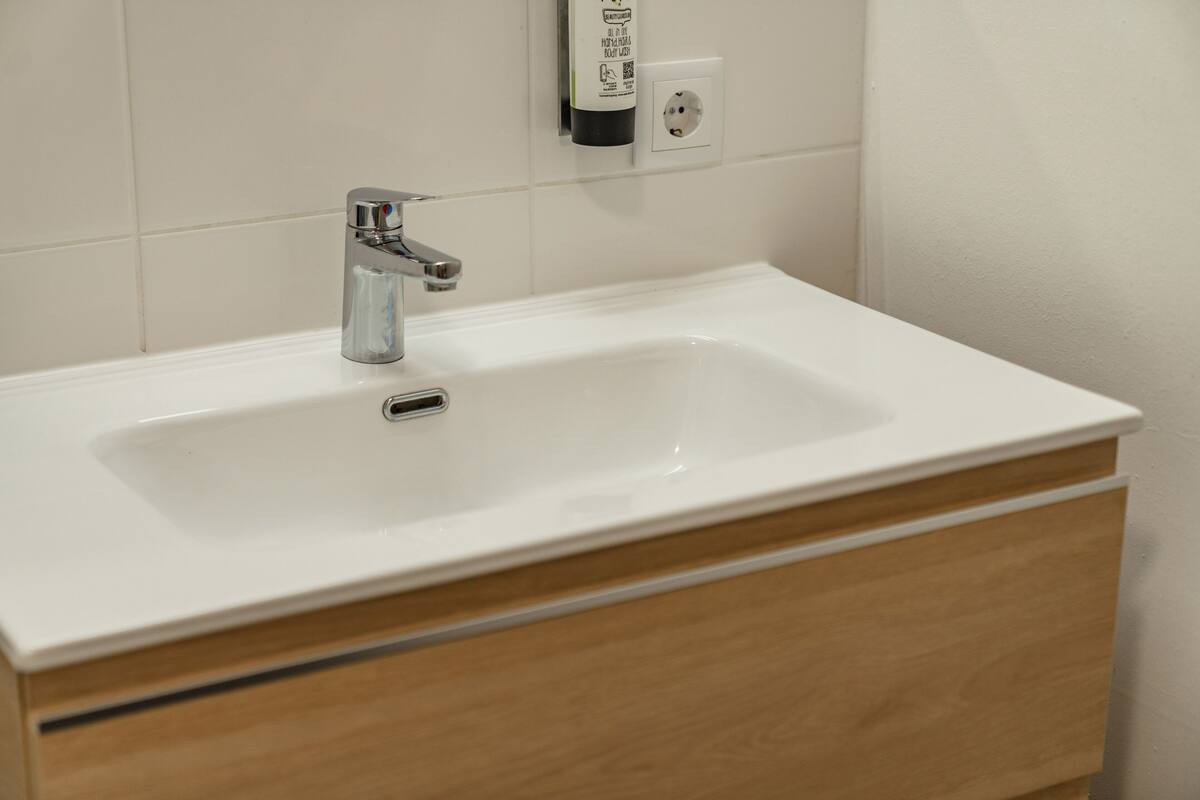 Baño con lavamanos blanco, grifo cromado y cajones de madera.