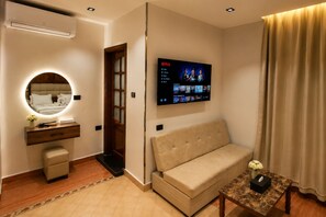 A modern hotel room with a sofa, a TV mounted on the wall, a vanity with a mirror, and a small table with a vase. - ZEINA PYRAMIDS VIEW HOTEL (Giza)
