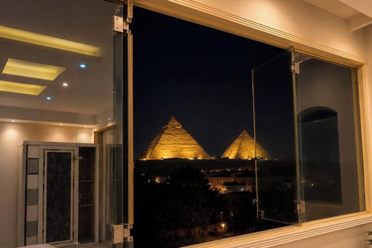 A room with a large window overlooking pyramids at night.