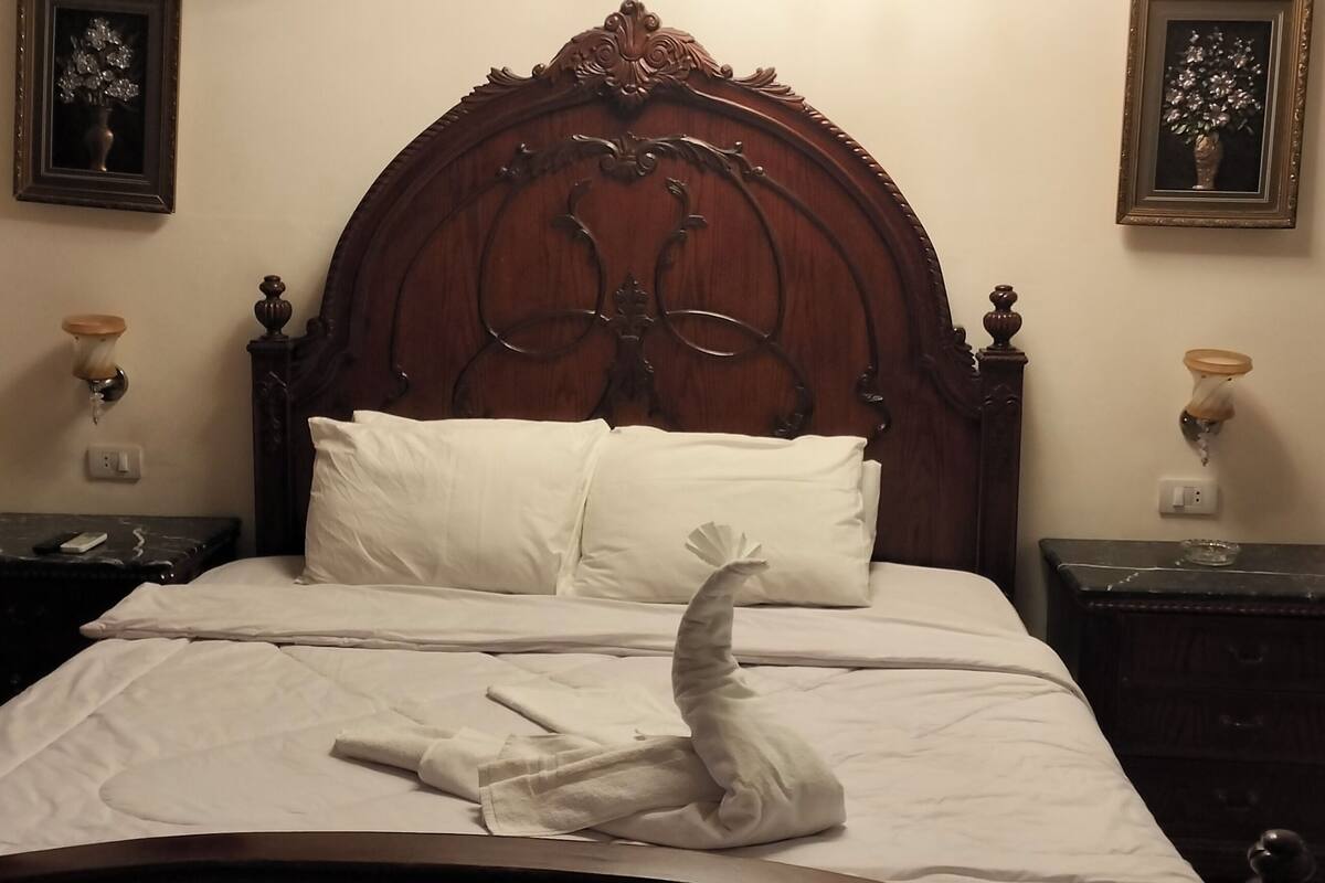 A bed with white linens, a wooden headboard, two bedside tables with lamps, and two framed pictures on the wall.