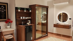Un baño moderno con tocador de madera, cabina de ducha con mampara de vidrio, espejo redondo y pequeño escritorio con silla.