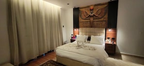 A hotel room with a large bed, a headboard with an Egyptian-themed design, a bedside table with a lamp, and a large window with curtains. - ZEINA PYRAMIDS INN (Giza)