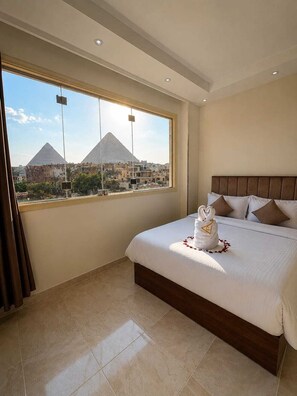 Habitació d'hotel amb un llit gran, vistes a les piràmides i una finestra amb cortines.