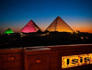 Tres pirámides iluminadas al anochecer, con un cartel que dice 'ISIS' en primer plano.