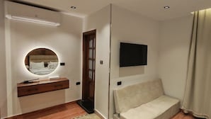 Un dormitorio con cama, mesita de noche, espejo, televisor montado en la pared y ventana con cortinas.