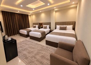 A hotel room with a large bed, a smaller bed, a sofa, a coffee table, and a minibar.
