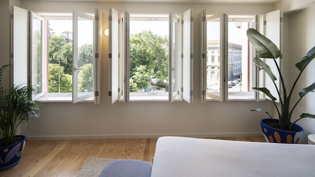 A bedroom with a large window, a bed, and two potted plants.