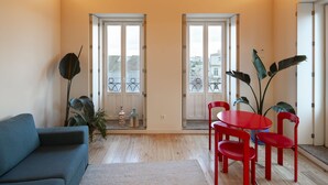A room with a sloped wooden ceiling, a blue sofa, a red table with chairs, and large windows with a city view.