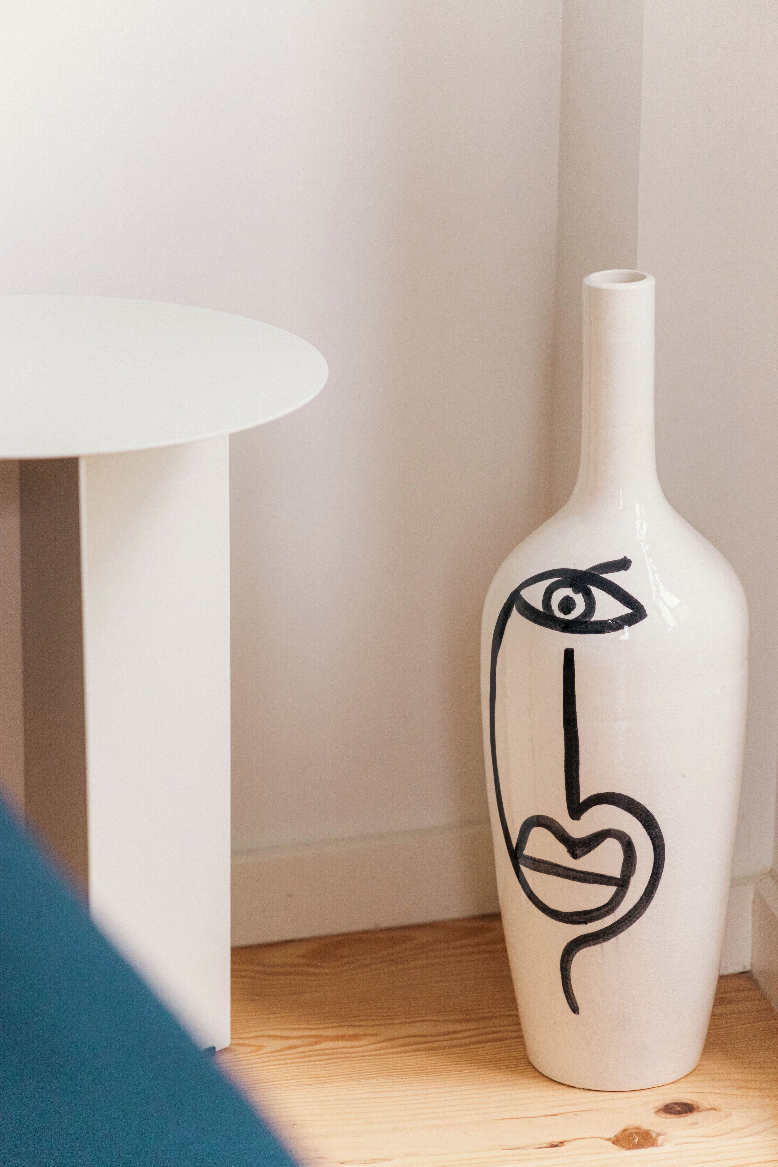 A white vase with a black drawing of an eye and a heart on a wooden surface.
