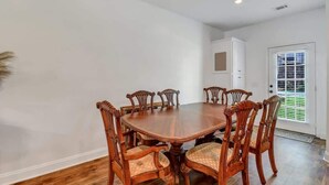 Une salle à manger avec une table ronde en bois entourée de six chaises, des murs blancs et une porte avec une fenêtre.