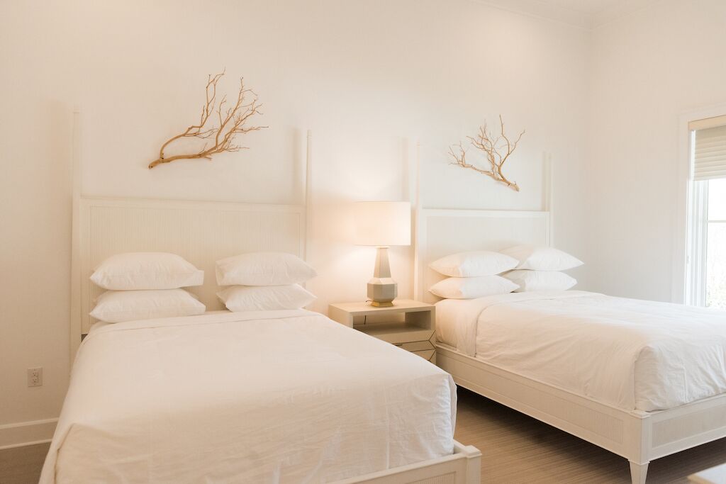 Una camera d'albergo con due letti, un comodino con una lampada e rami decorativi sulla testiera.