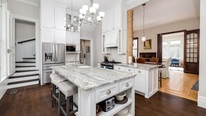 A spacious kitchen with white cabinetry, a granite island, and a staircase leading to another level.