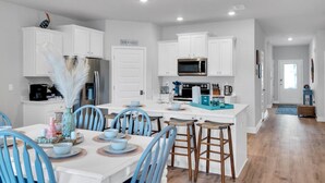 A modern kitchen with white cabinets, a central island with stools, and a dining area with blue chairs. - 🏖️1st Row Beach House🌴6 Seat Golf Cart 🌊OceanView Pools🏝️Beach Equip🔥Patio-Firepit (Port St. Joe)